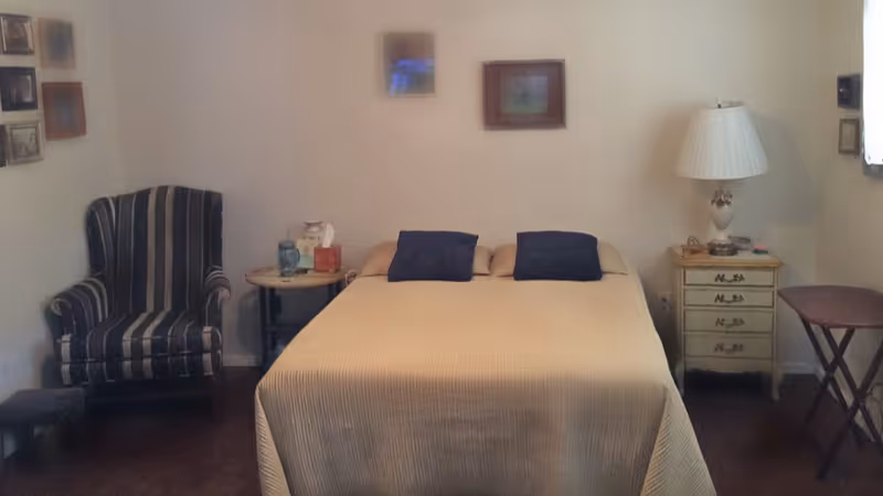 A bedroom with a bed, nightstand, lamp, and striped armchair.