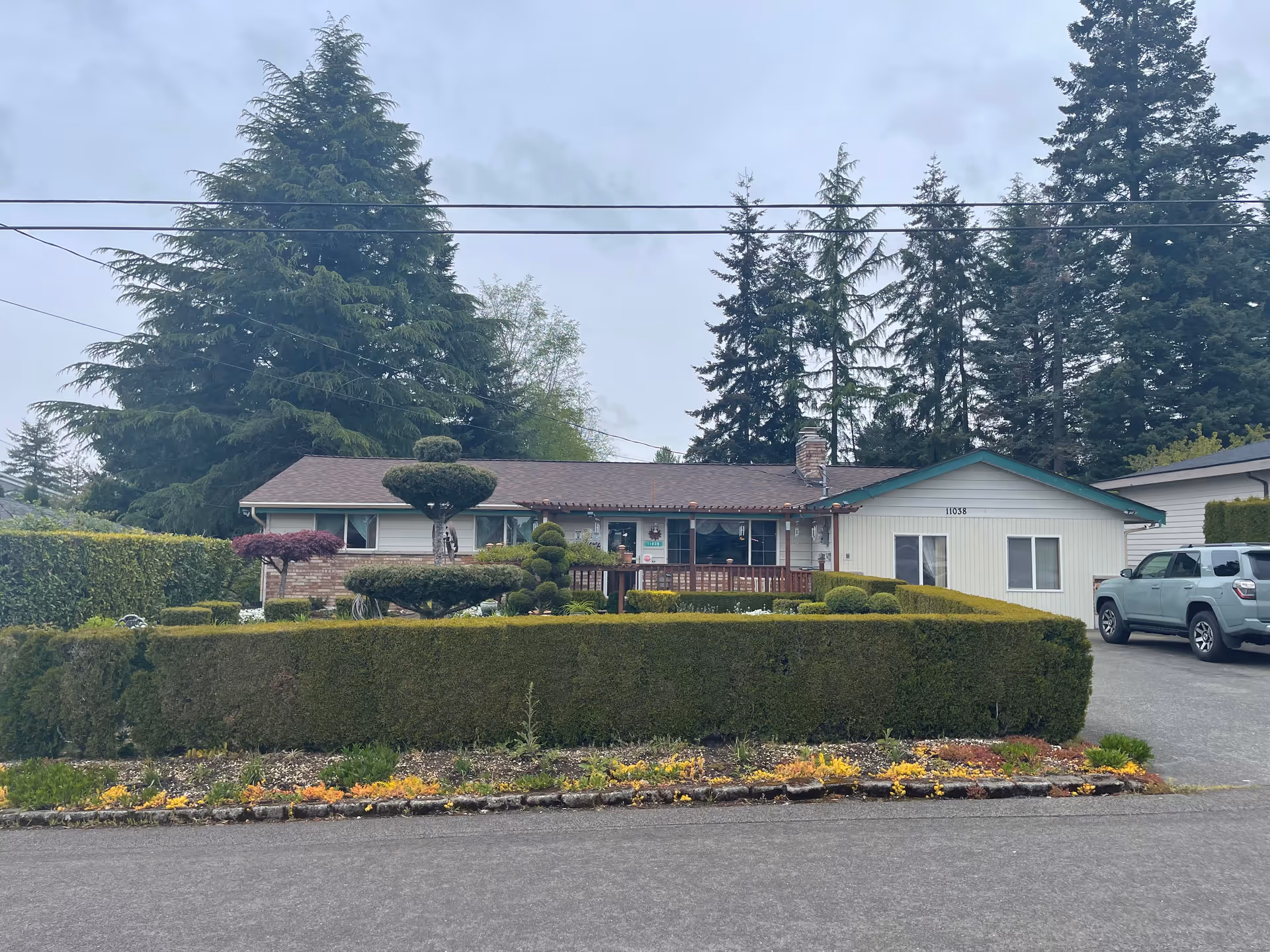 Single-story building with manicured hedges, driveway, and a parked SUV in front.
