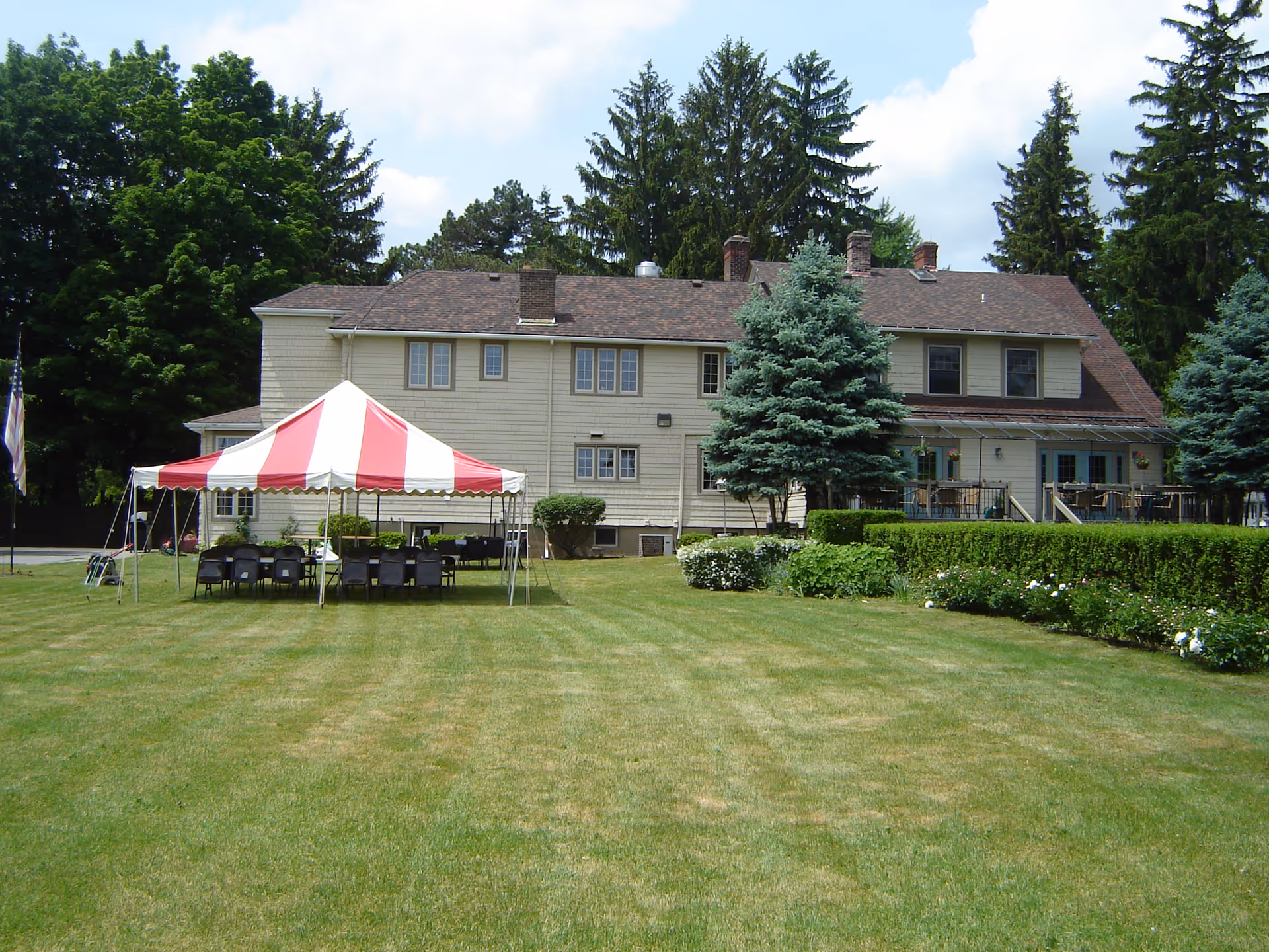 Green lawn with a red and white striped tent in front of a two-story building.