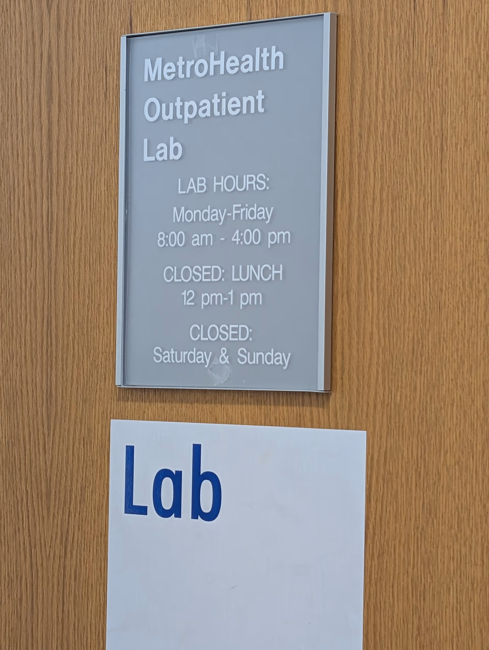 MetroHealth Outpatient Lab sign with hours mounted on wood panel