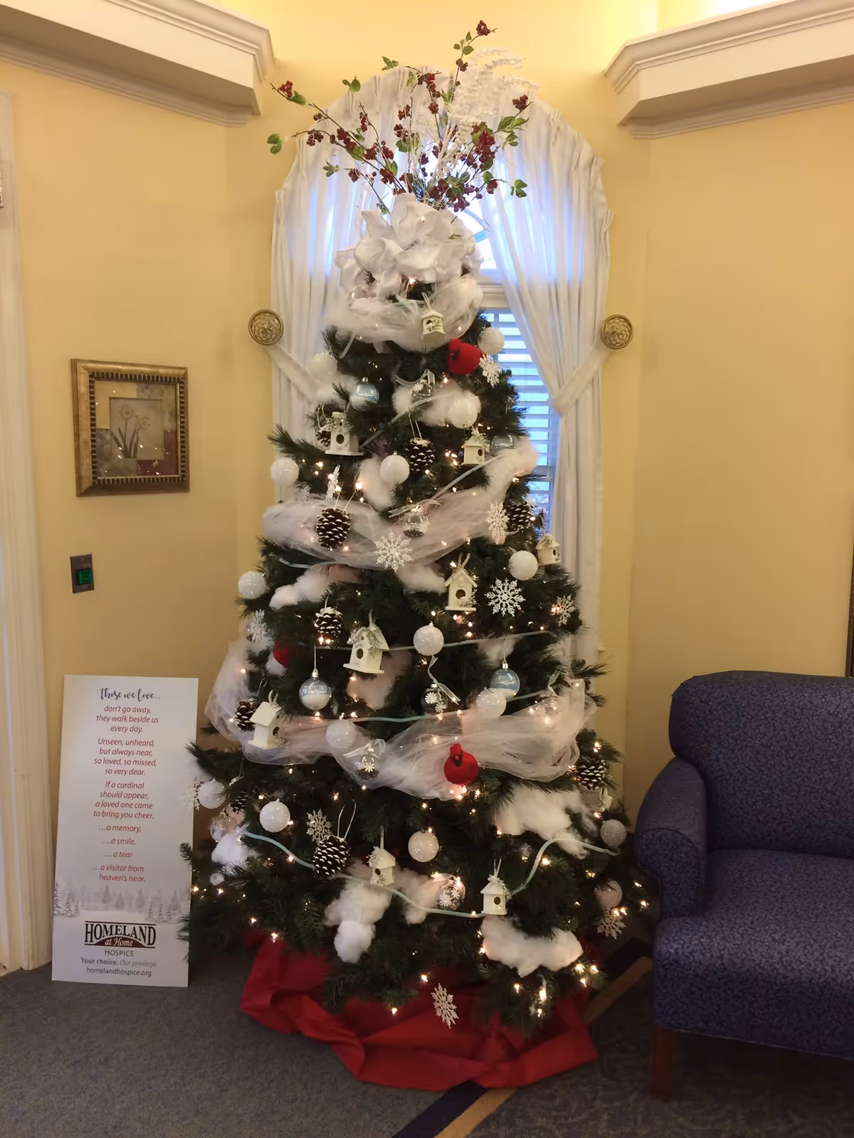 A decorated Christmas tree with white ornaments sits in a warmly lit indoor lobby.
