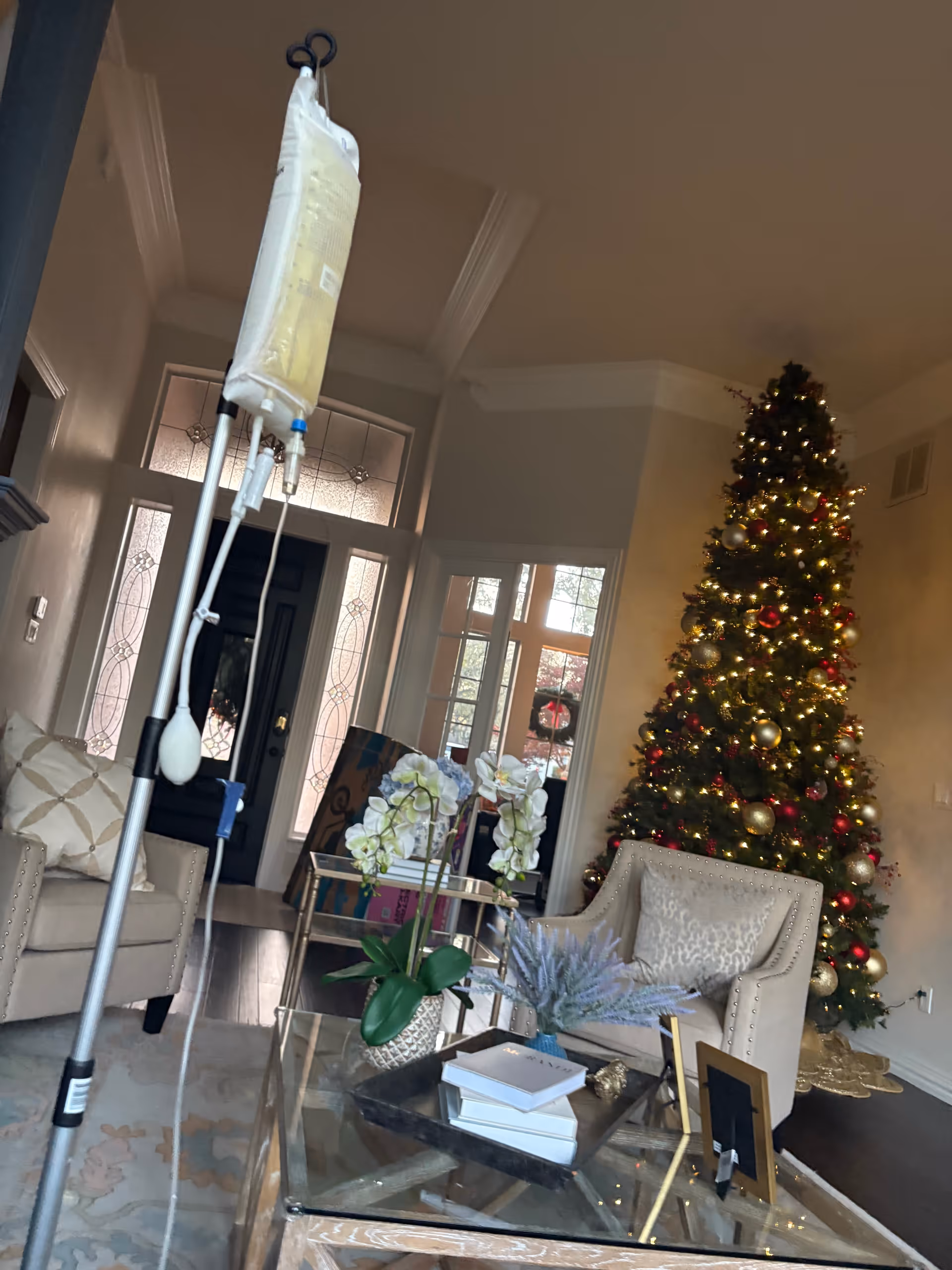 A living room with a decorated Christmas tree, white furniture, and an IV stand.