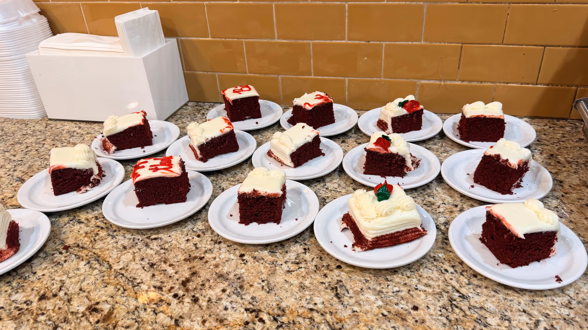 Several red velvet cake slices on individual plates arranged on a granite counter.