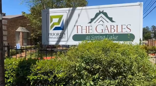 Entrance sign reading 'The Gables at Spring Lake' with a Priority Management logo in front of shrubs and a brick building.