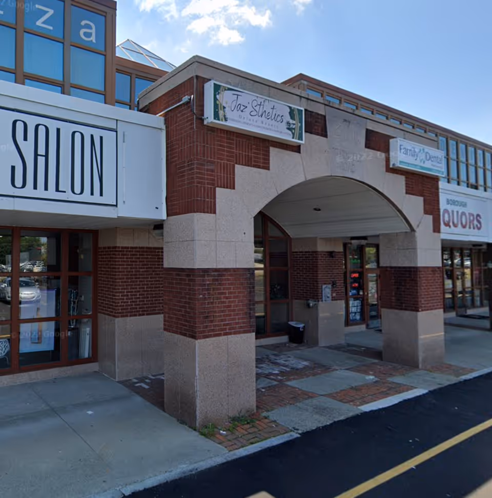 Exterior view of a brick storefront building with arched entrance and shop signs.