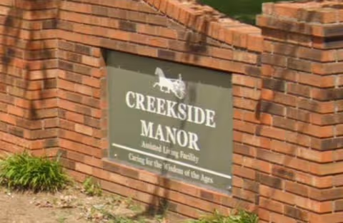 Brick entrance wall featuring Creekside Manor Assisted Living Facility sign with logo and landscaping