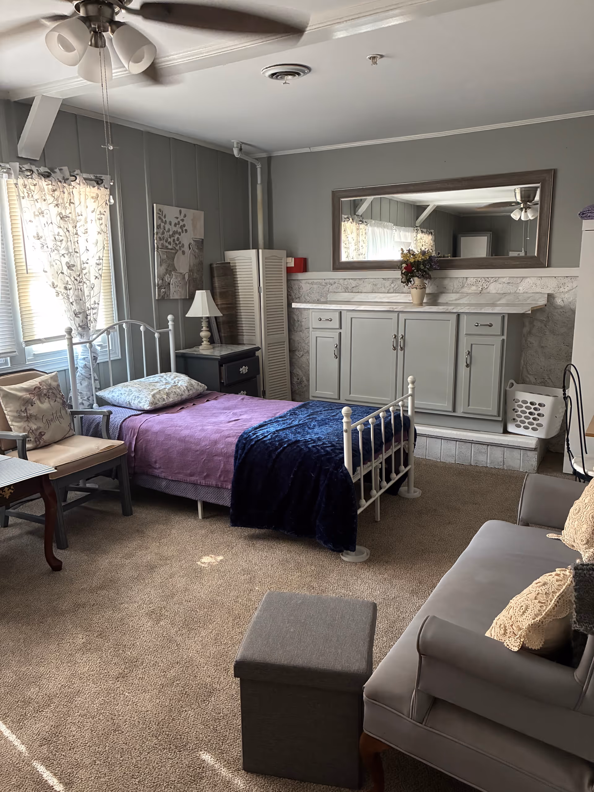 Cozy resident bedroom with bed, dresser, seating area, and ceiling fan.