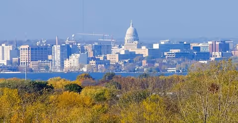 City skyline with a domed capitol building seen behind autumn trees.