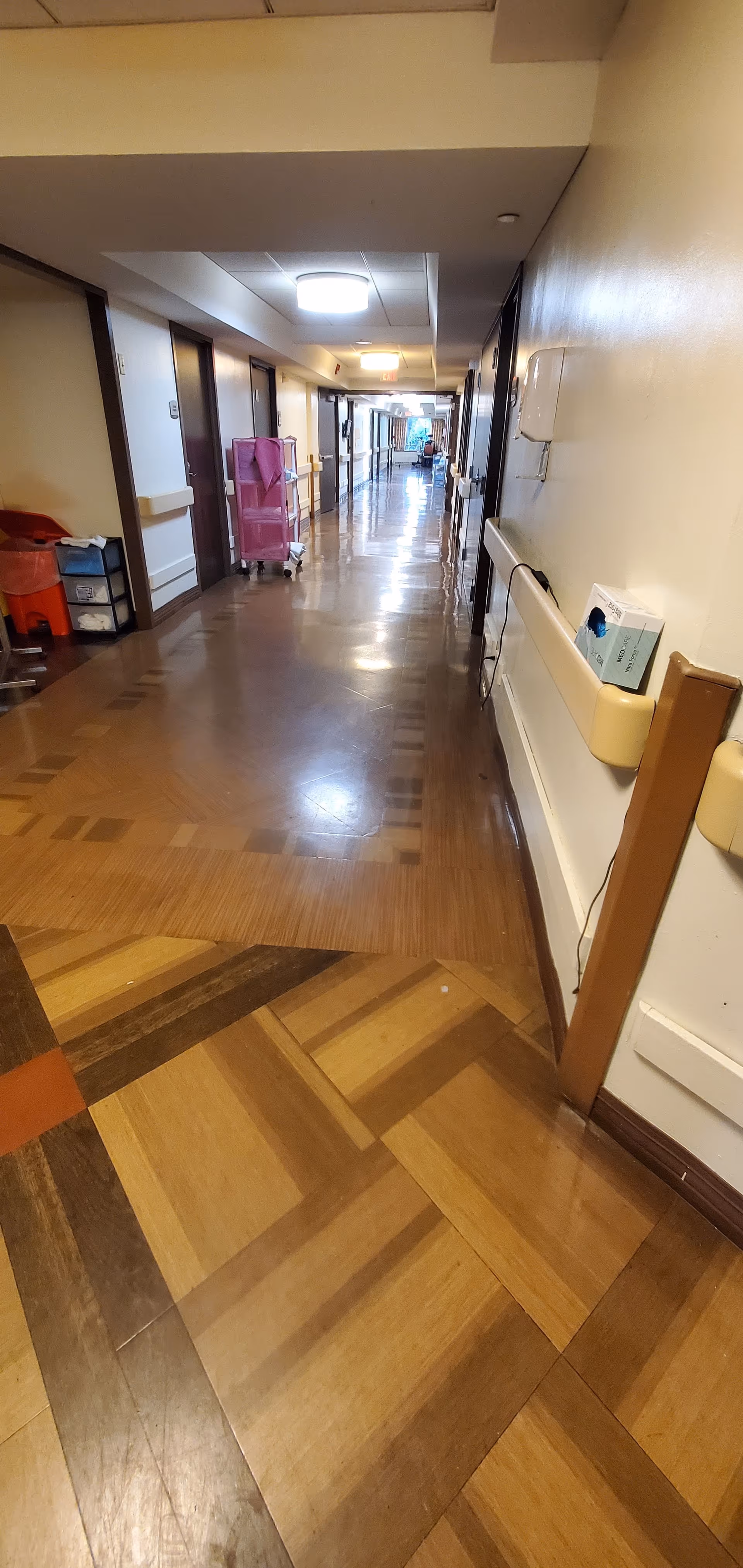 Long interior hallway in a senior living facility with doors along both sides and carts.