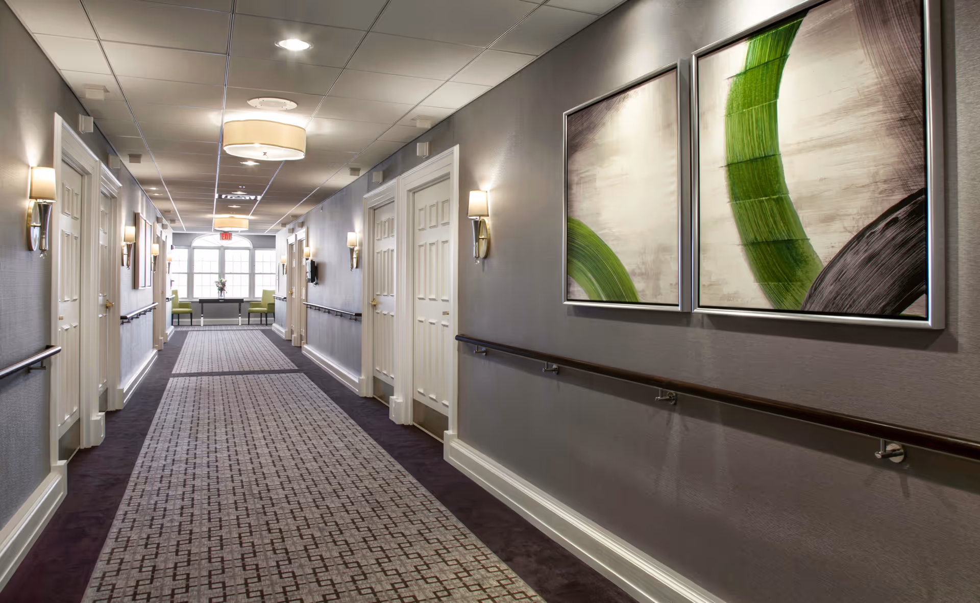 A well-lit hallway of a senior living facility with chairs visible at the far end.