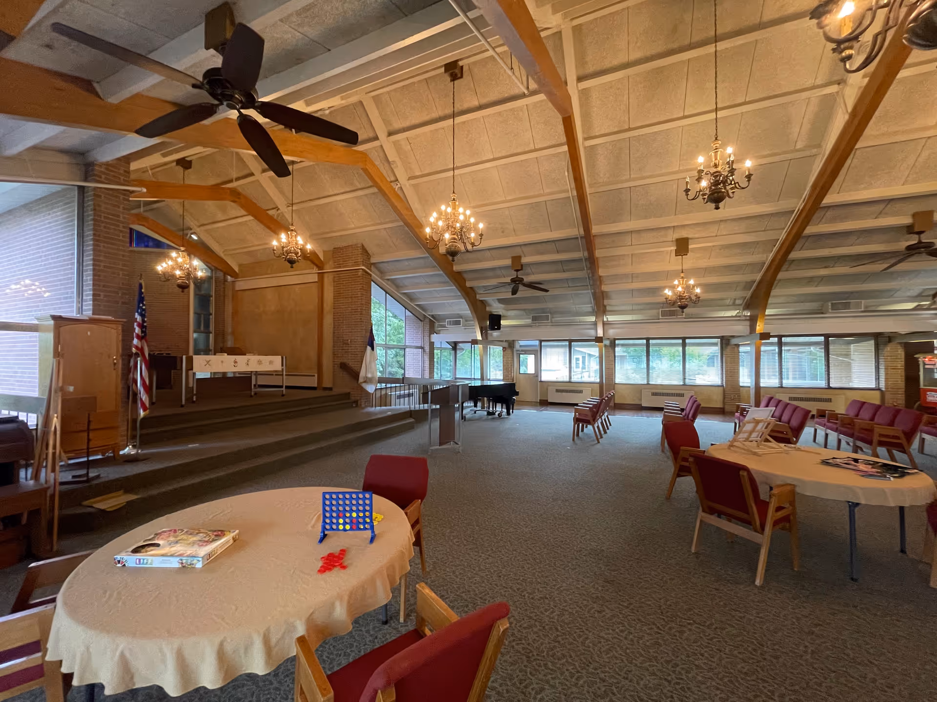 Large indoor hall with round tables, chairs, chandeliers, and a stage area.