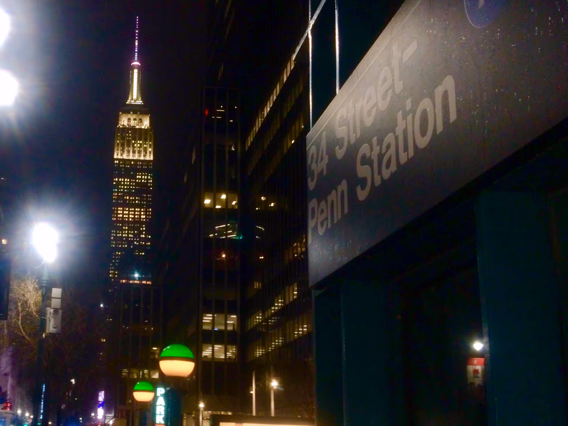Nighttime city street with lit Empire State Building and Penn Station sign on building