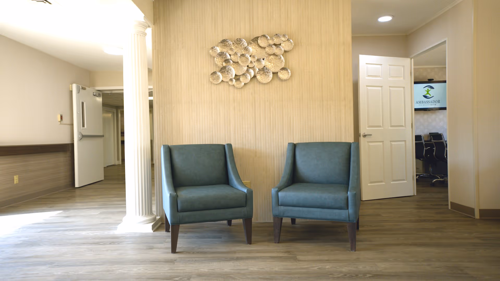 Lobby seating area with two teal chairs and doorway to offices