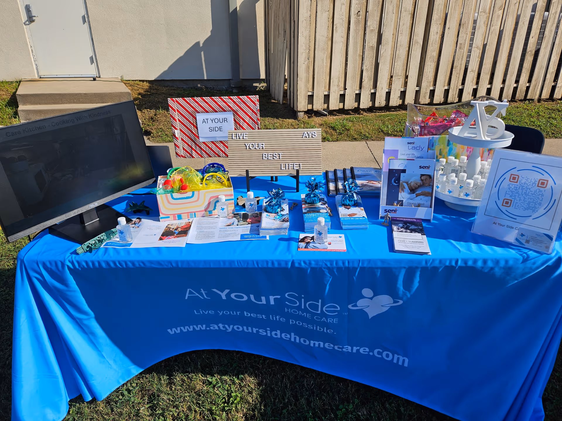 Outdoor promotional table with blue cloth, brochures, and displays for At Your Side Home Care.
