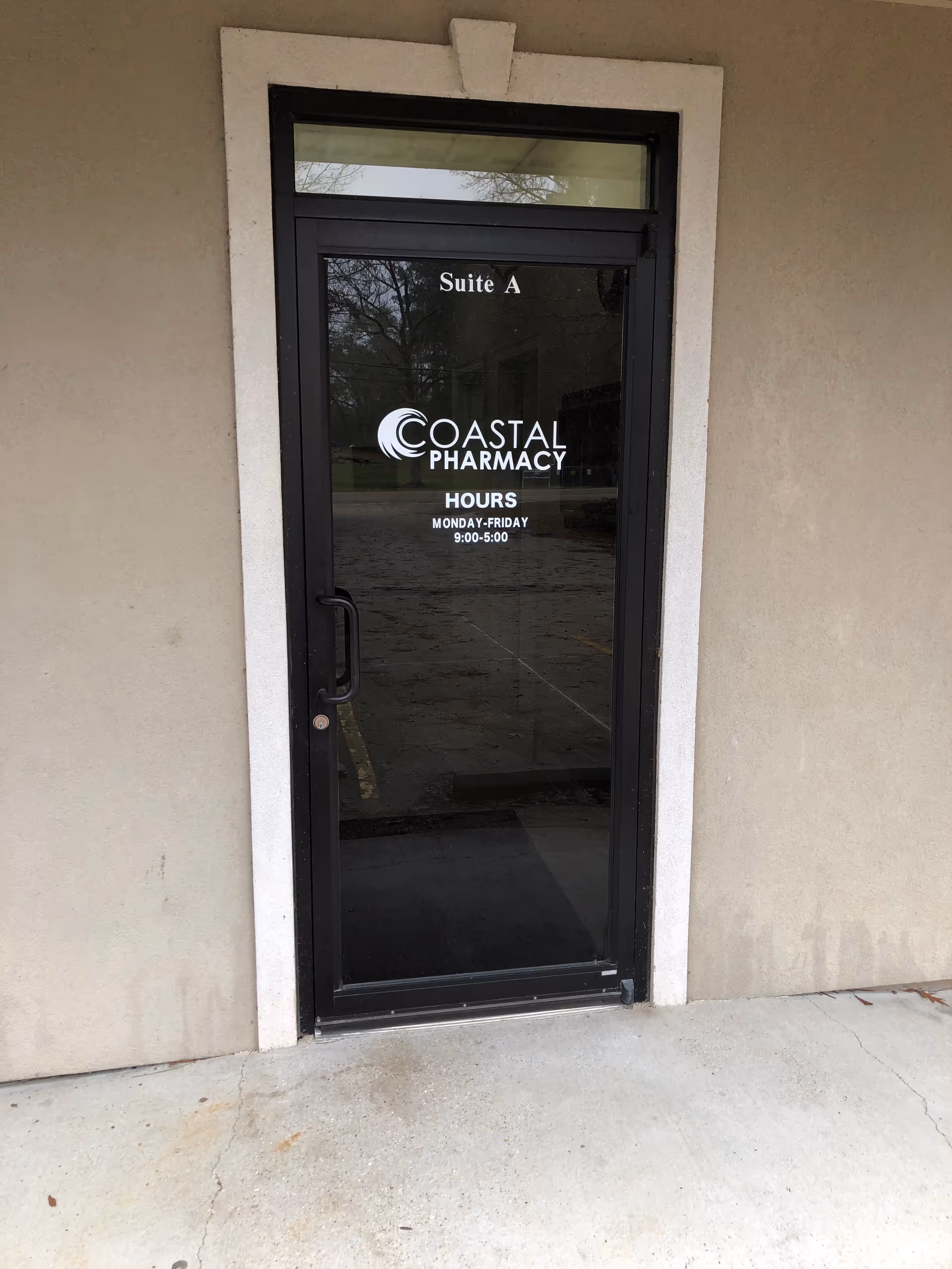Glass door labeled Suite A with Coastal Pharmacy signage, set in beige exterior wall.