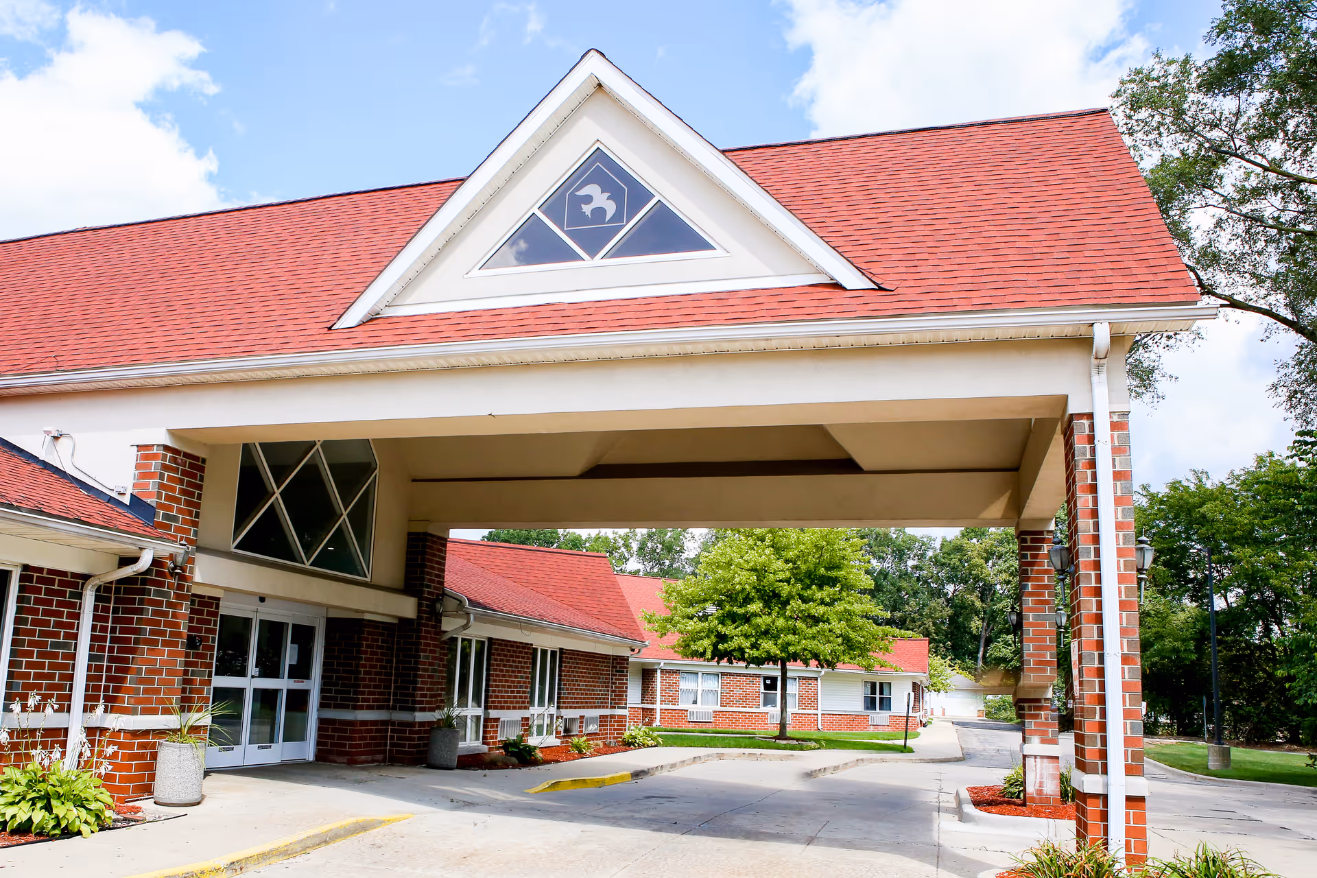 Red-brick senior living facility entrance with a covered drive canopy and landscaping.