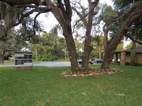 Lawned outdoor area with trees, a sign, and a parking lot visible.