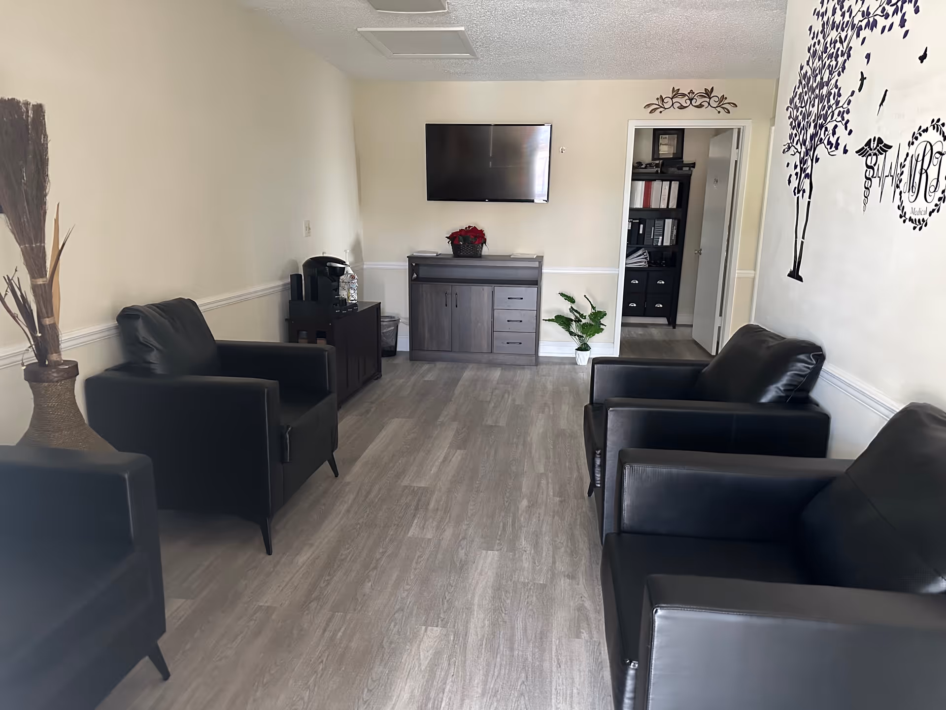 A modern senior living lounge with black leather chairs, a wall TV, and a cabinet.