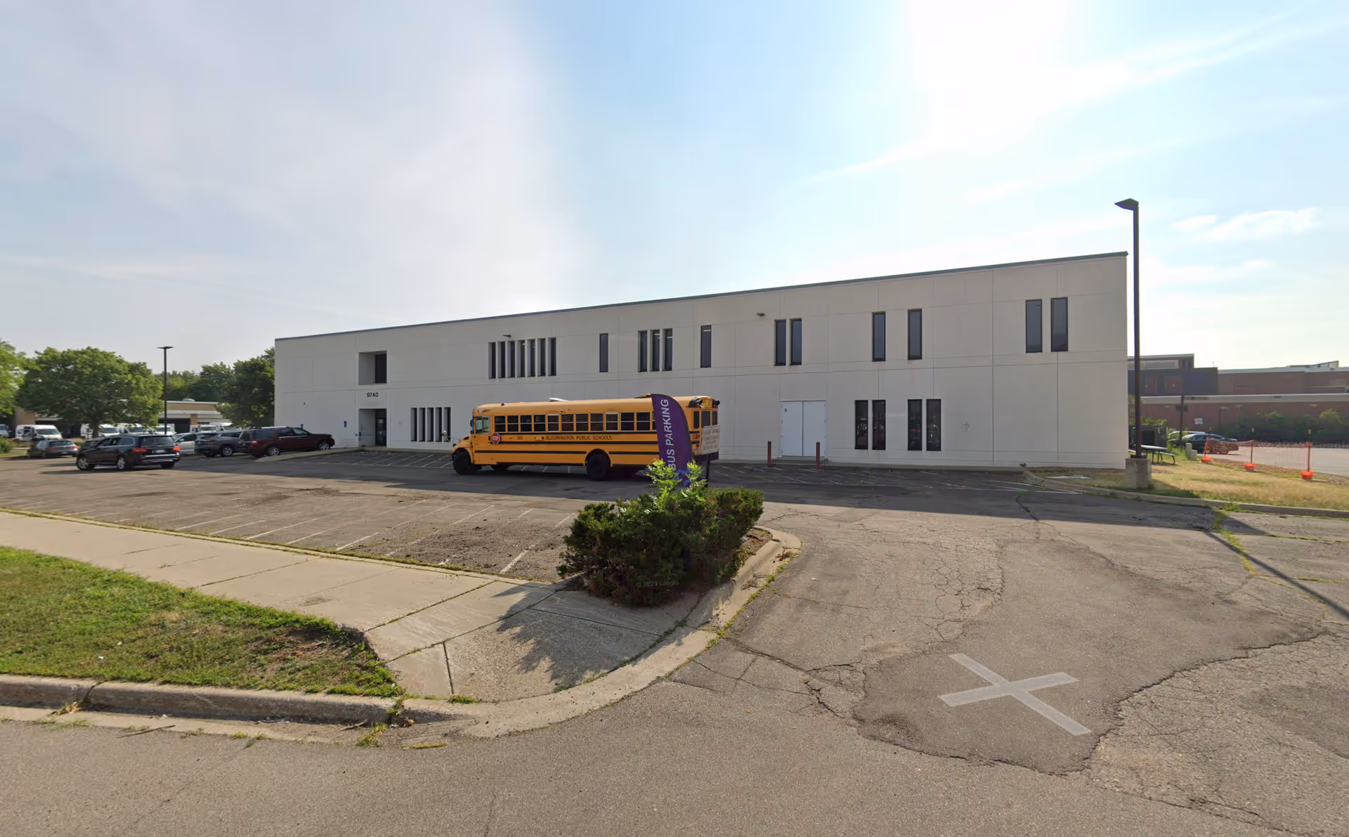 A white modern senior care facility exterior with a parking lot and a yellow school bus