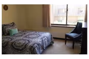 A bedroom with a patterned bed, window, and a chair beside the window.