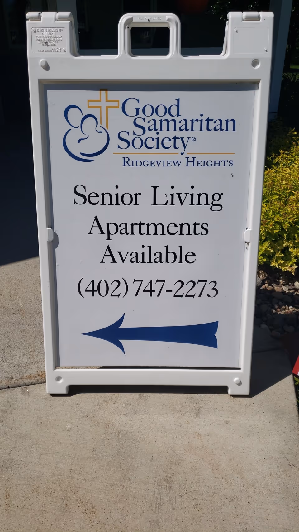 White sidewalk sign for Good Samaritan Society Ridgeview Heights Senior Living Apartments available with blue arrow.