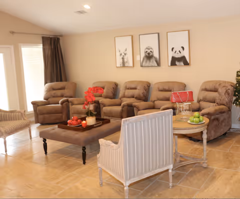 A cozy living room with a row of brown recliners, upholstered chairs, a central ottoman with decor, and three framed animal prints on the wall.