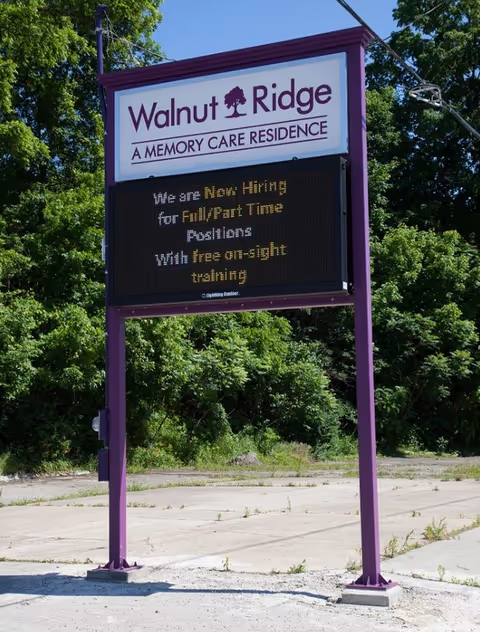 A freestanding purple-framed sign for Walnut Ridge Memory Care Residence with an electronic message board in front of trees.