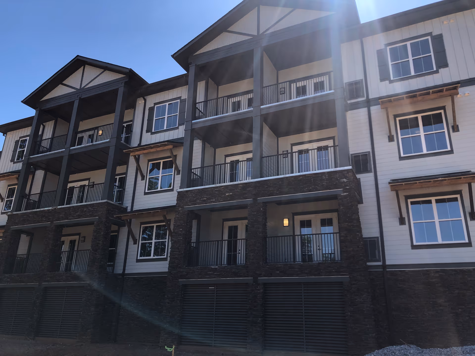 Three-story residential building with balconies and stone accents under a clear blue sky.