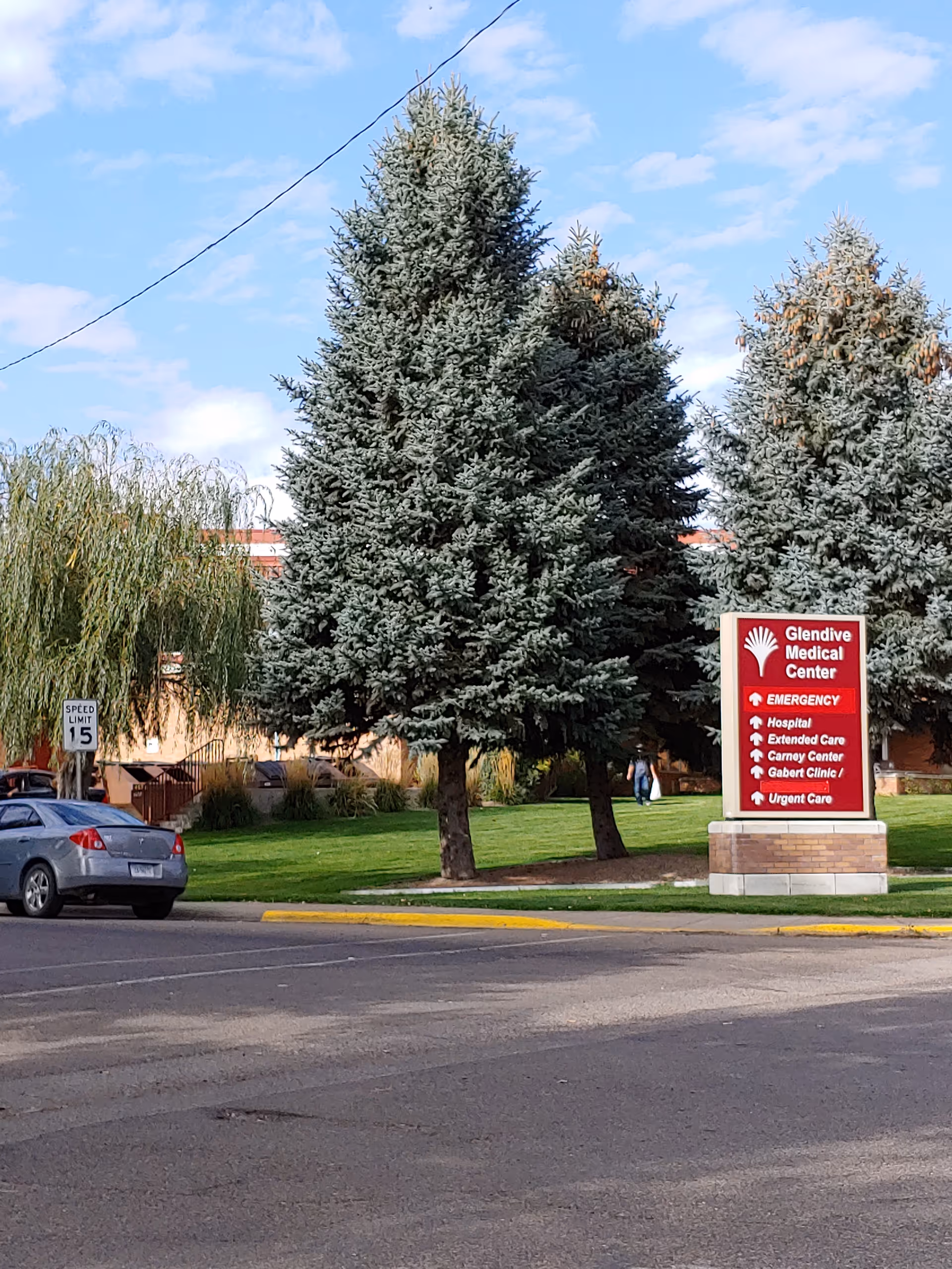 A street view shows a Glendive Medical Center sign, tall evergreen trees, and parked cars.