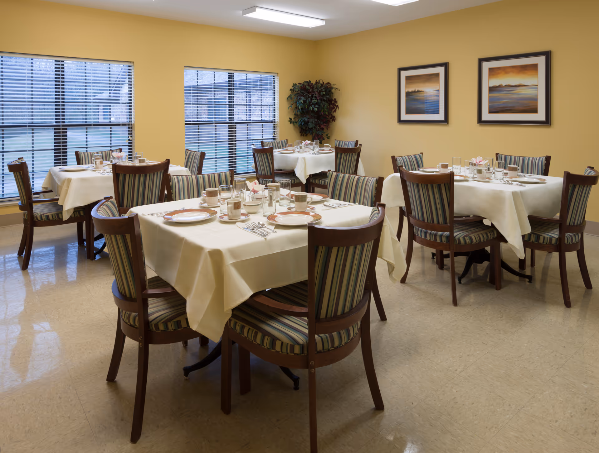 Bright dining room with tables set for meals and striped chairs.