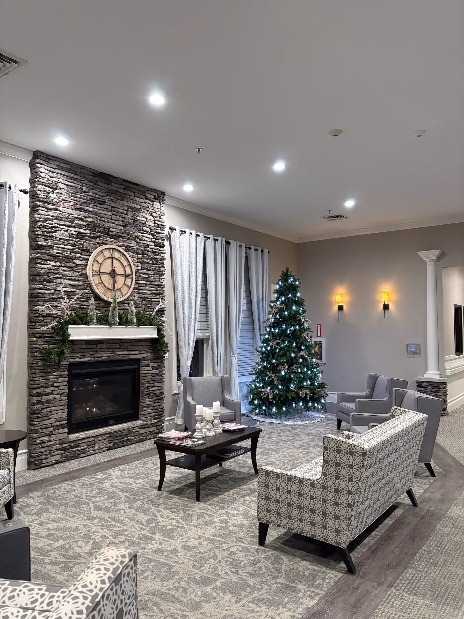 Cozy senior living lounge with stone fireplace, Christmas tree, and seating area.