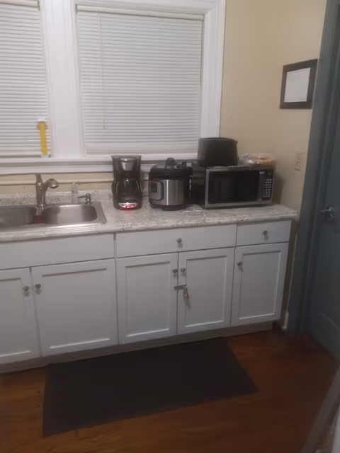 Small kitchen counter with sink, coffee maker, microwave, and appliances along white cabinets.
