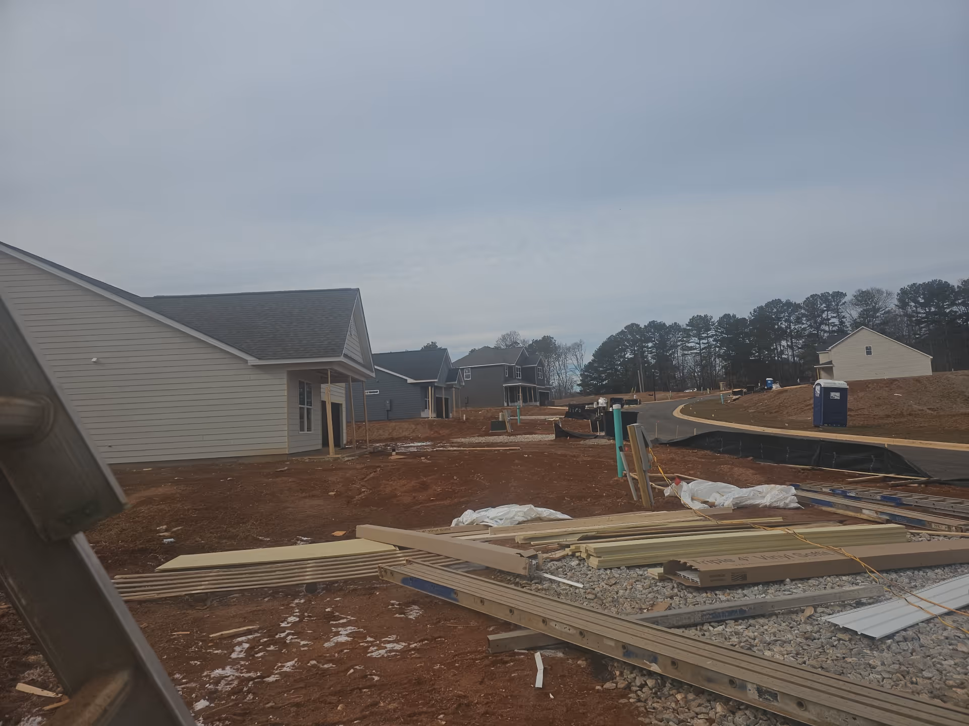 Under construction residential development with partially built homes and muddy lots along a curved street.