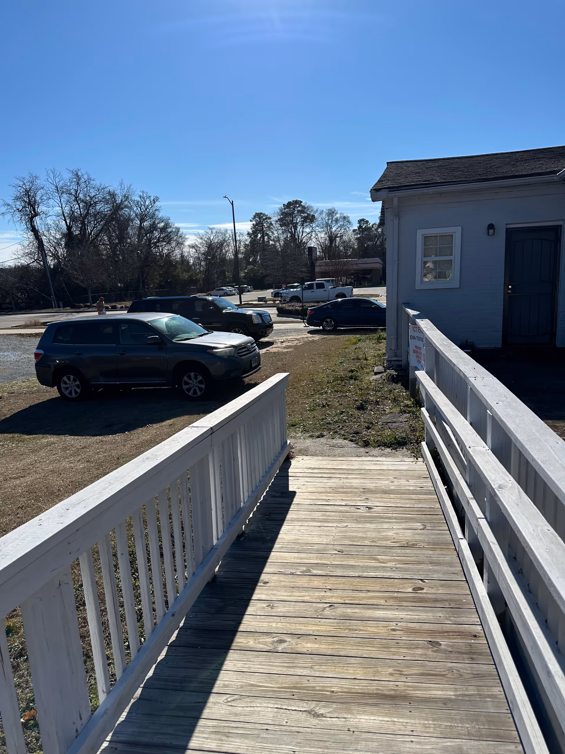 Exterior view of a wooden ramp with white railings leading to a small building.