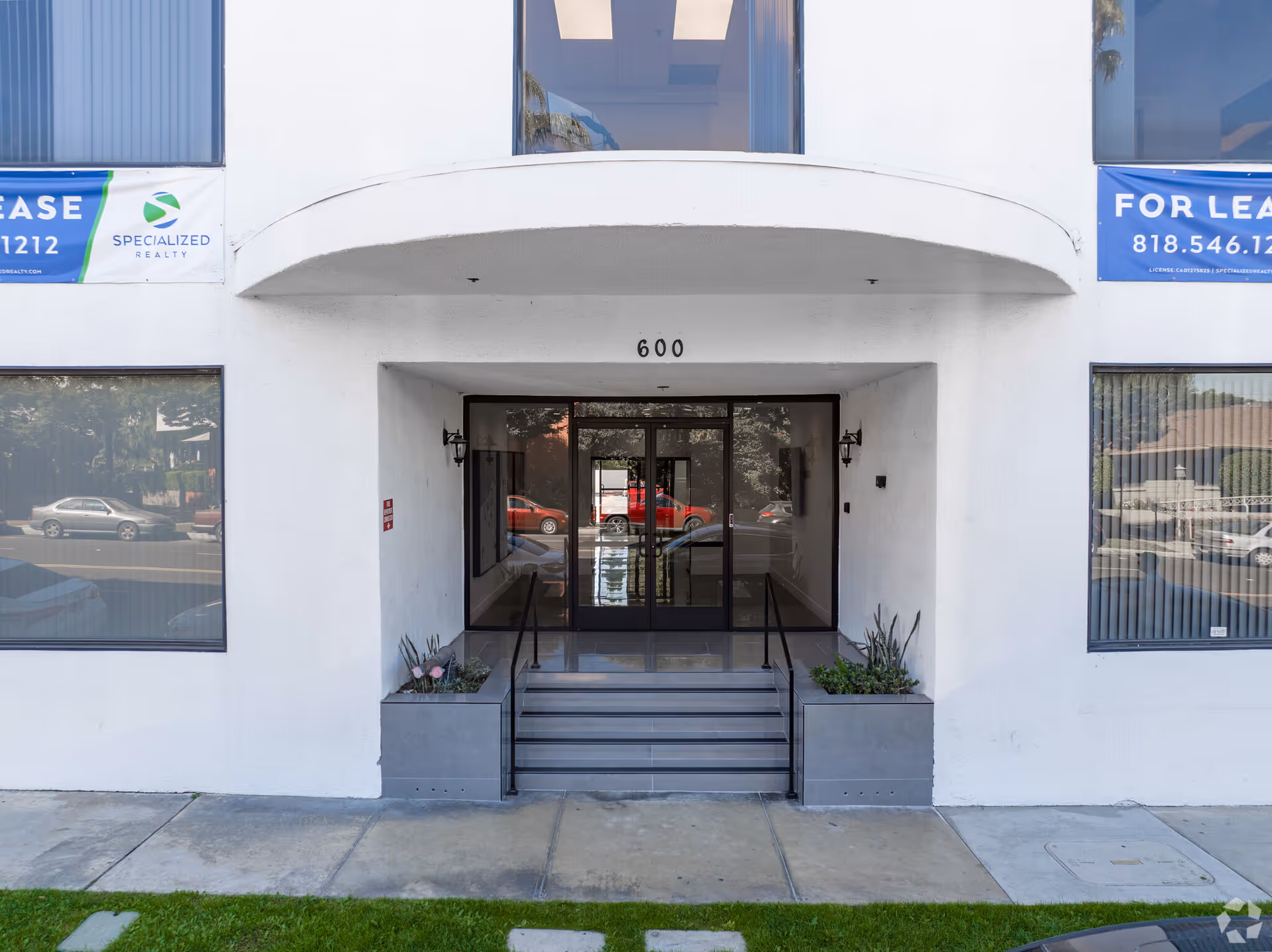 White commercial building with glass doors, stairs, planters, and the number 600 above entrance.