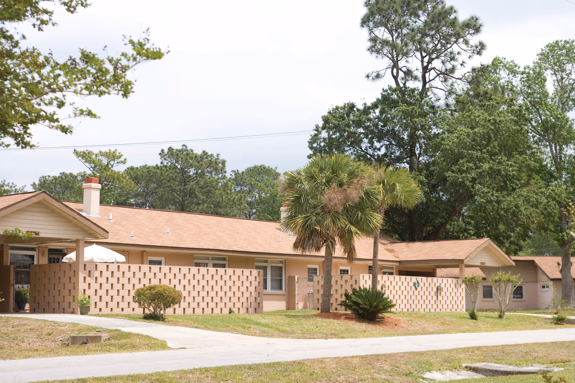 Single-story beige Cecil Pines Adult Living building with lattice walls, palm trees, and a driveway.