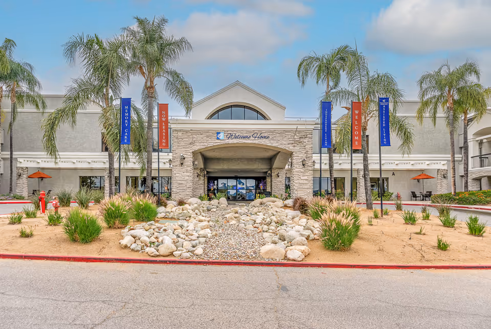 Exterior view of Open Arms 20 V senior living facility entrance with palm trees and landscaping.