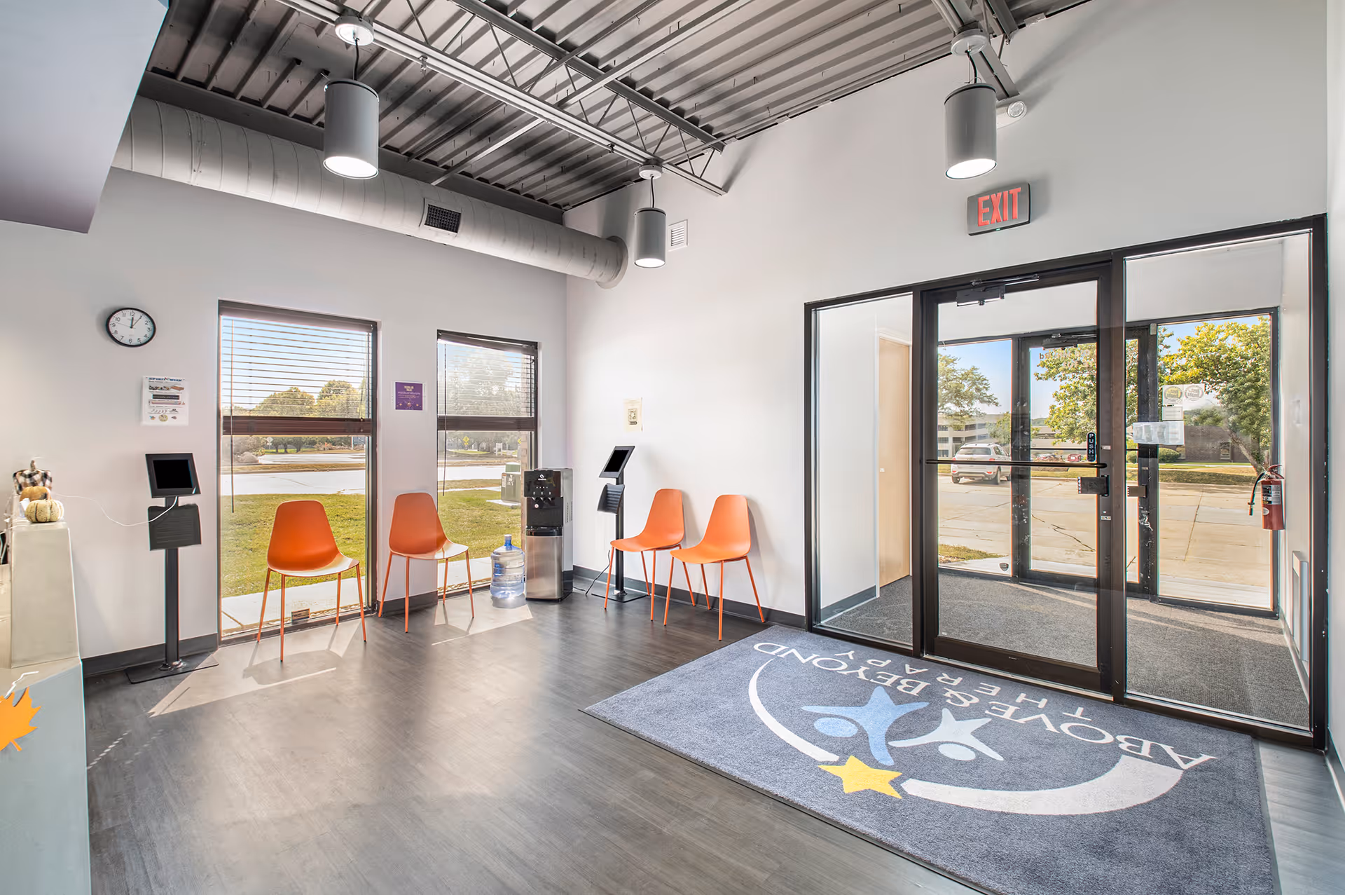 Interior lobby with orange chairs, glass doors, a rug, and an exit to the outside
