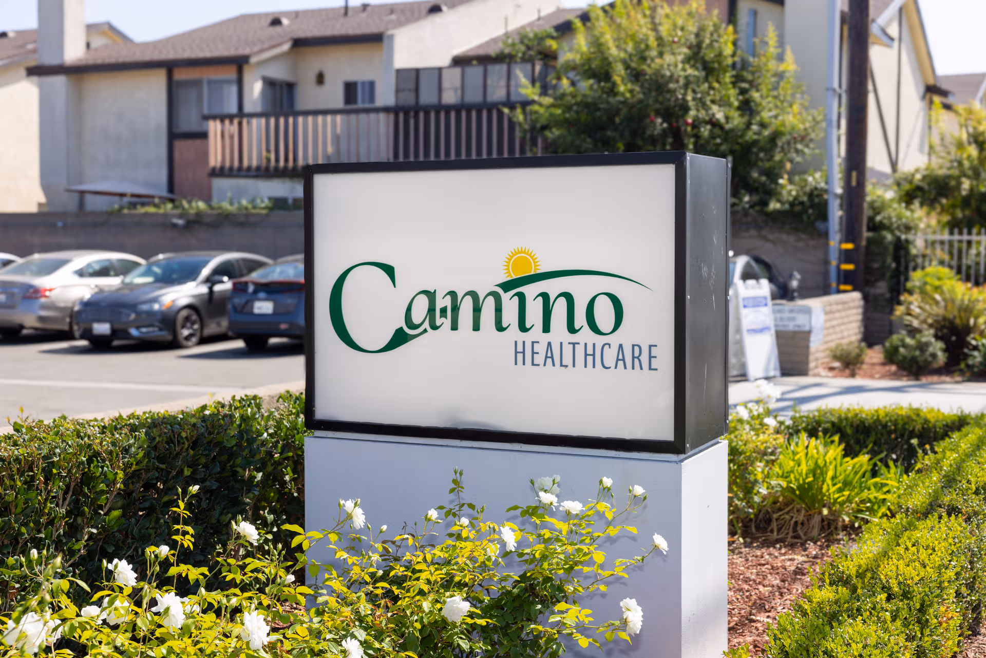A Camino Healthcare sign in front of a parking lot and residential building.