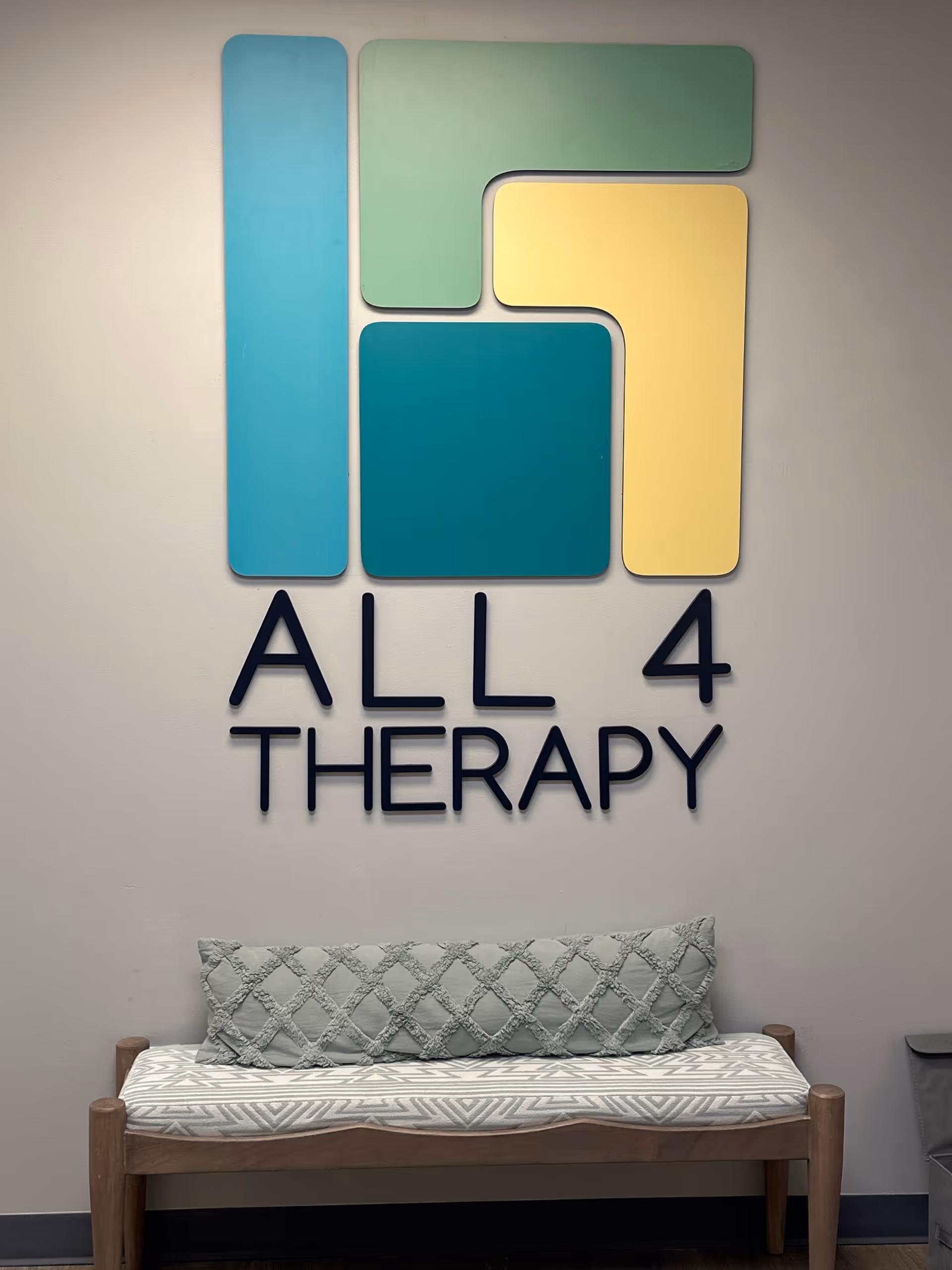 Lobby-style interior with a bench and a large colorful All 4 Therapy logo on the wall.