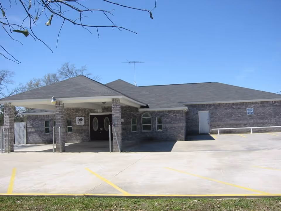 Exterior view of a brick senior living facility with a covered entrance and parking.