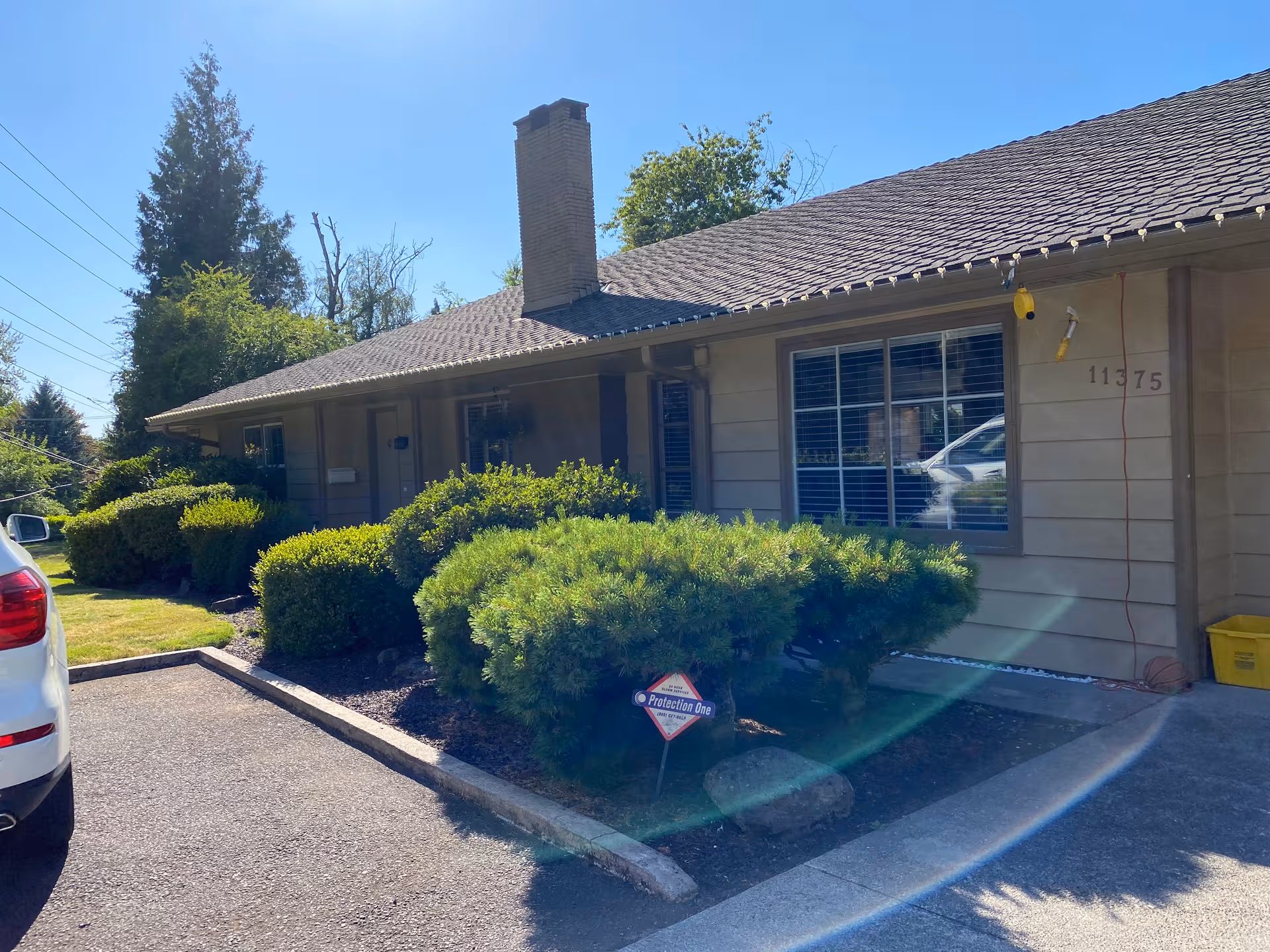 Front exterior of Capitol Adult Care Home with shrubs and a driveway on a sunny day