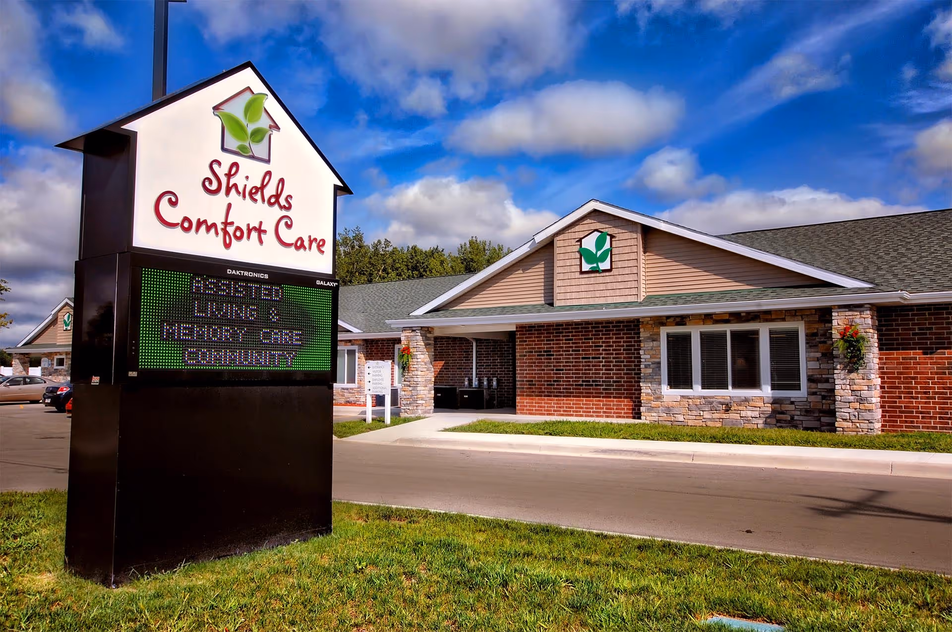 Exterior view of Shields Comfort Care assisted living building with a large roadside sign in front.