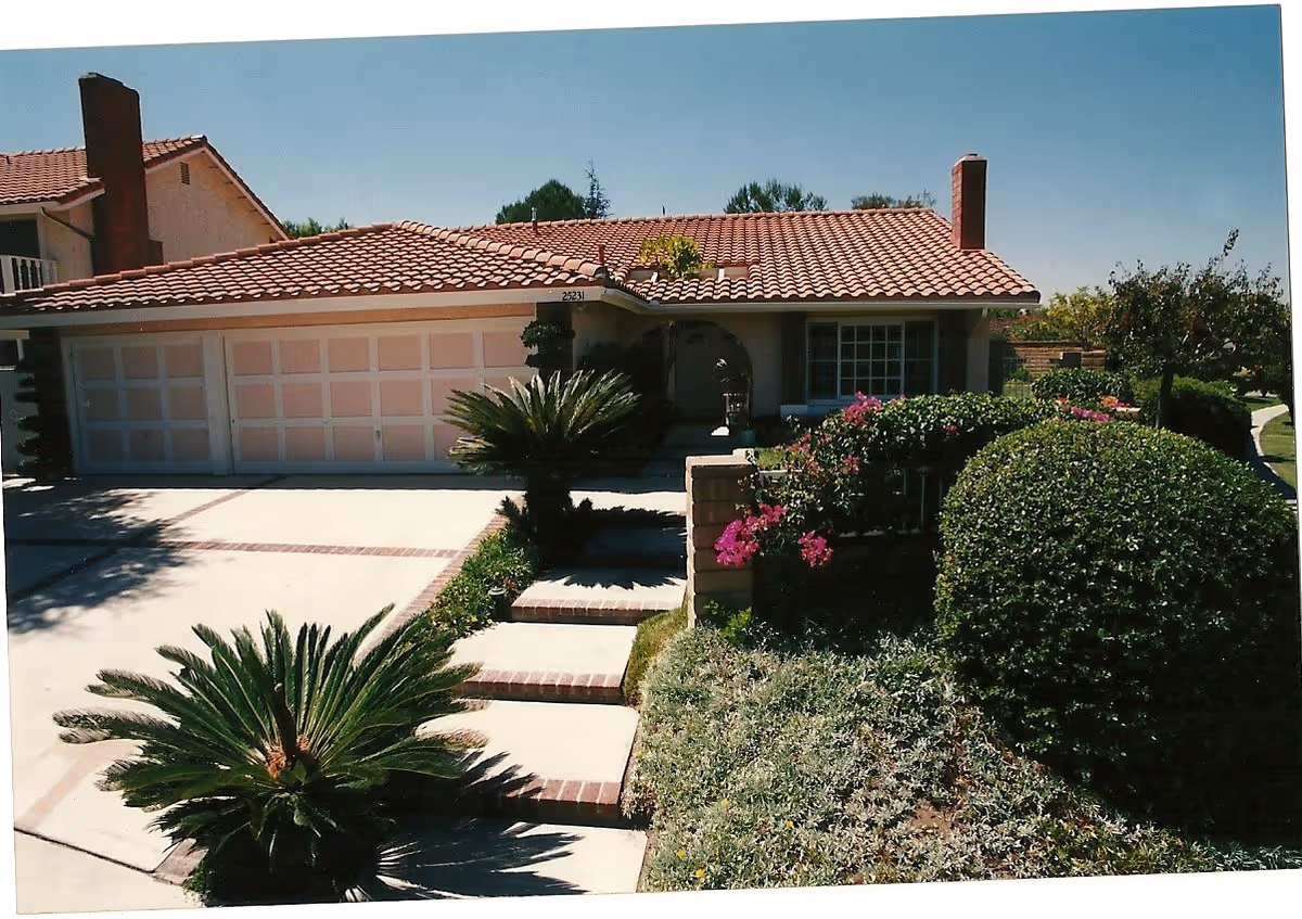 Single-story house with a tiled roof, three-car garage, and a landscaped front yard with steps, shrubs, and flowering bushes.
