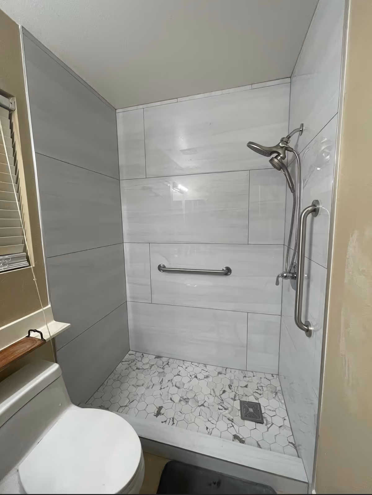 Walk-in tiled shower with grab bars and a toilet in a compact bathroom.