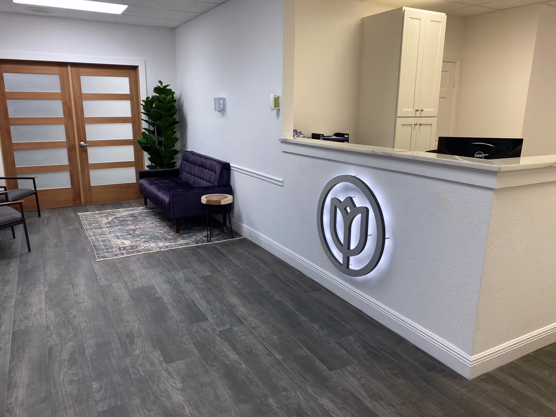 Modern reception area with a circular logo, white counter, purple sofa, and double doors.