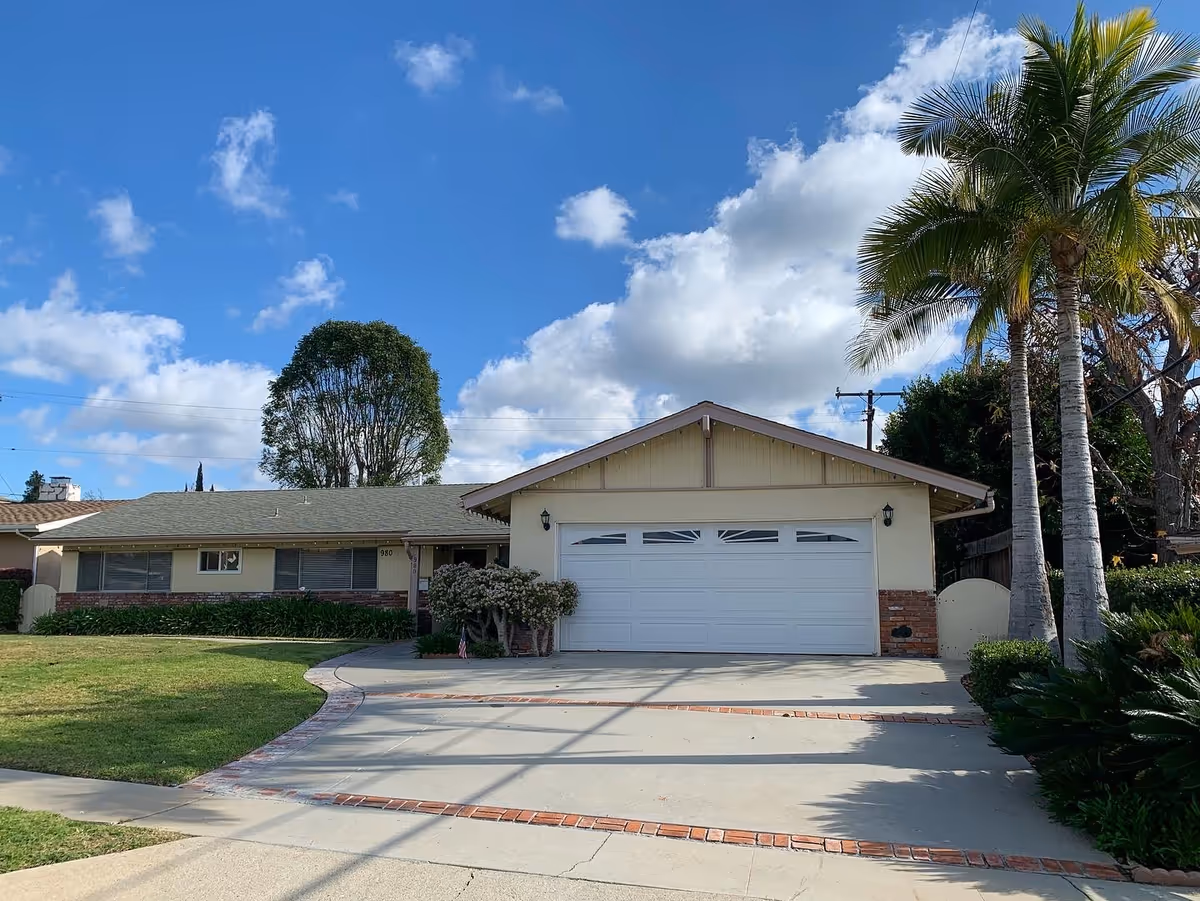 Front exterior of a single-story home with a two-car garage and palm trees.