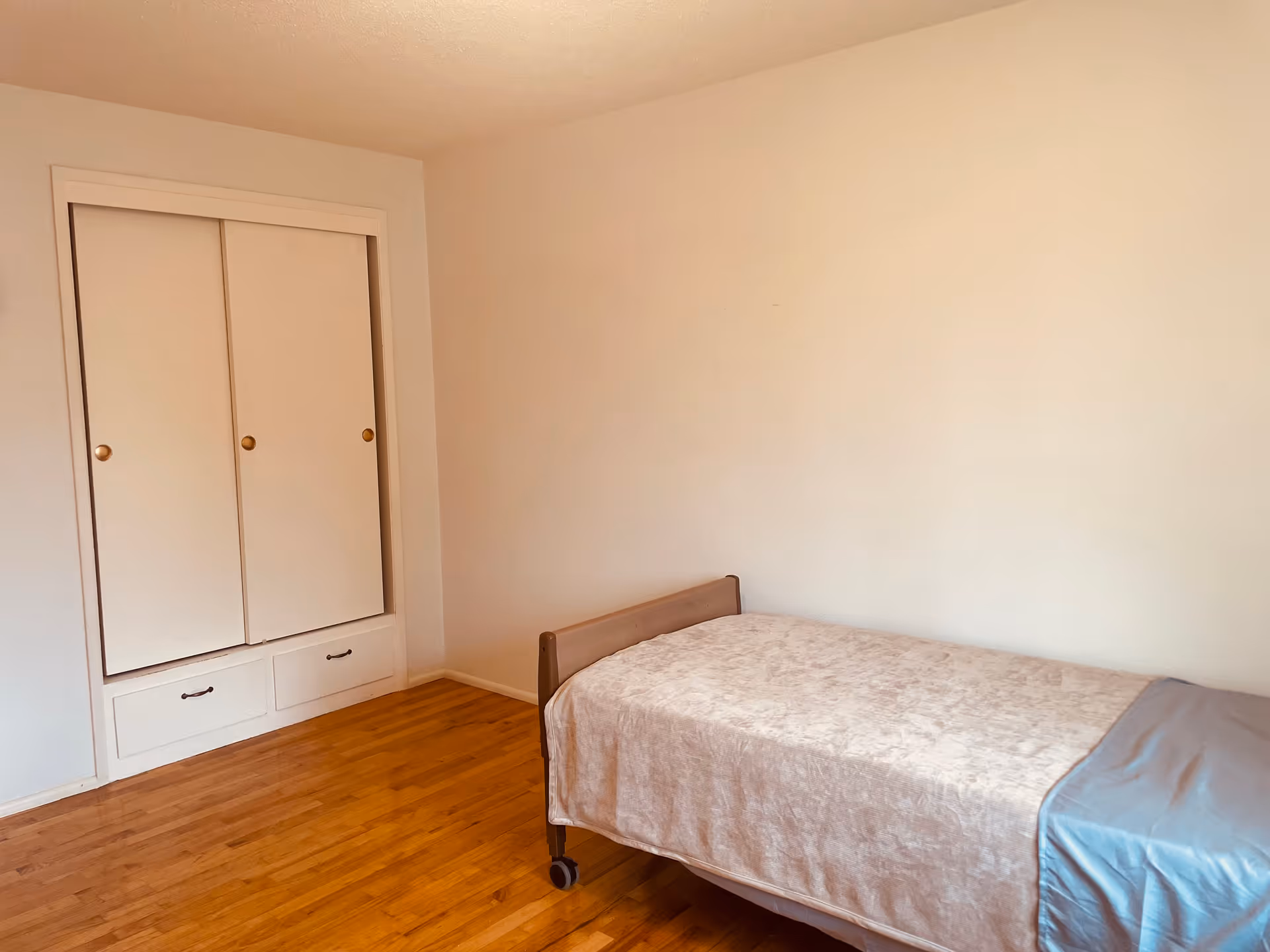 A simple bedroom with a single bed, built-in wardrobe, and wooden floor.