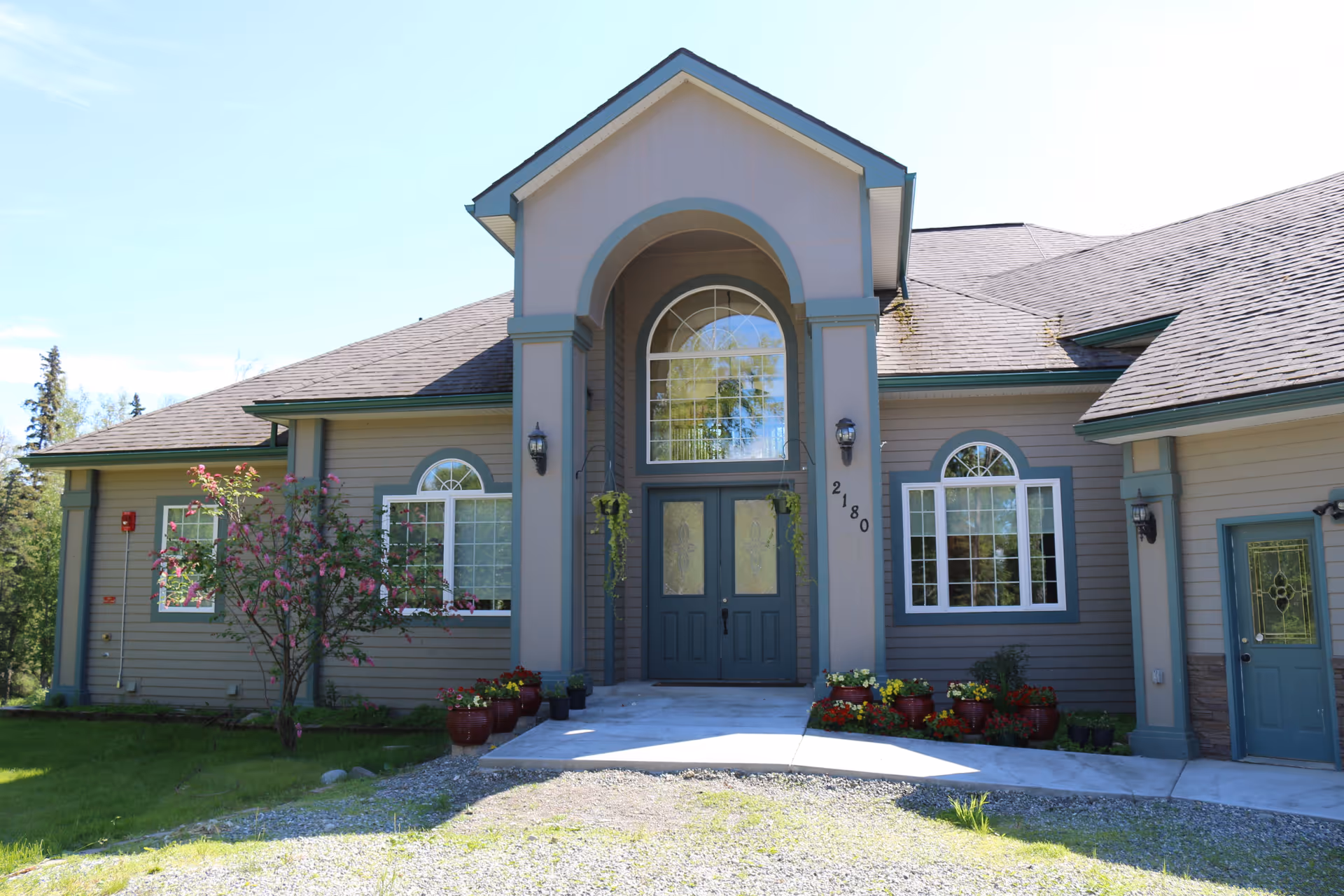 Front view of a gray senior living facility with arched entrance and potted plants