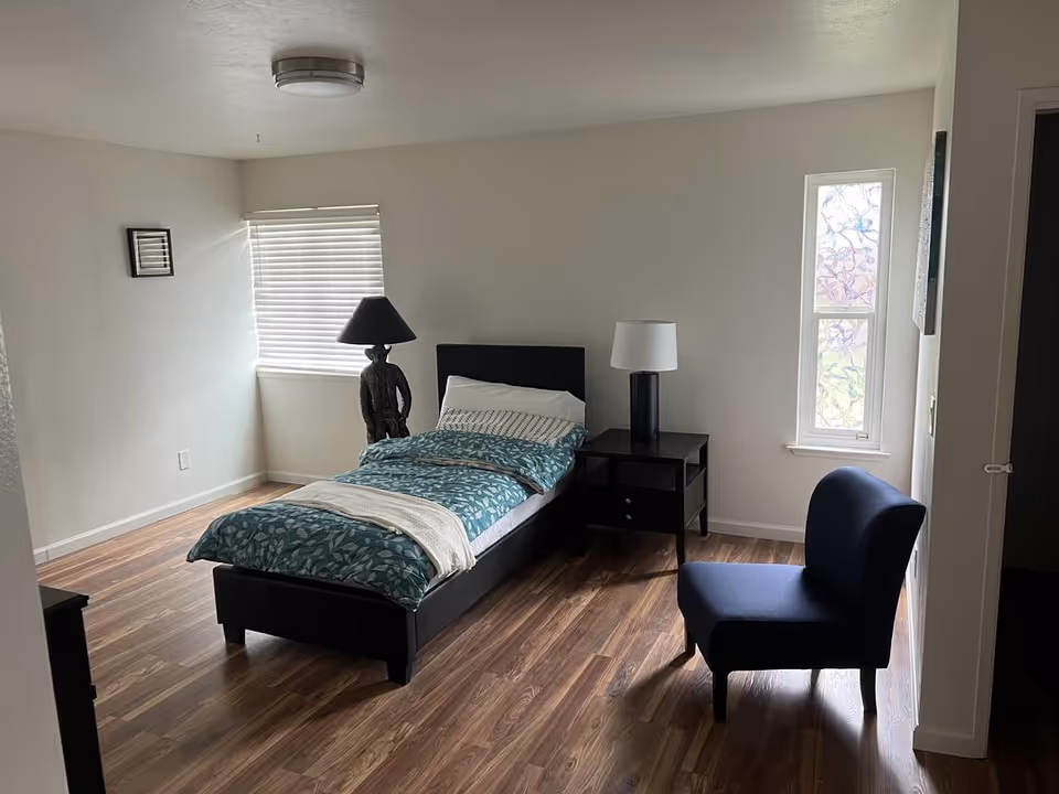 Bedroom with bed, nightstands, two lamps, blue bedding, and a blue chair.